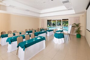 Sala de conferências com mesas preparadas para uma reunião, um projetor e vista para a piscina externa.