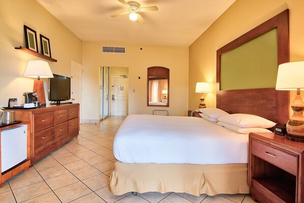 A hotel room with a bed, bedside tables, a television, a desk with a lamp, and a mirror.