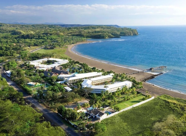 An aerial view of a coastal resort with multiple buildings, a beach, and a pier.