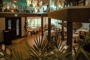 A multi-level restaurant with tables and chairs, a reception desk, and a staircase.