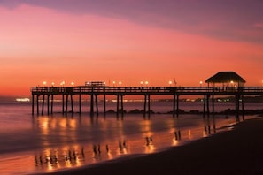 A pier extending into calm waters at dusk with a covered seating area and lights along its length.