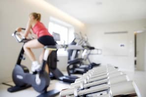 A gym with exercise equipment and a person using an elliptical trainer. - Schweizerhof (Lucerne)