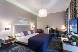 A hotel room with a bed, desk, chair, and a decorative wall with a car silhouette. - Schweizerhof (Lucerne)