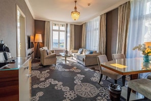 Habitación de hotel con sofá, sillas, una mesa de comedor, televisor y ventana con cortinas.
