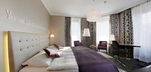 A hotel room with a large bed, a desk, and a chair. There is a quote on the wall and a chandelier. - Schweizerhof (Lucerne)