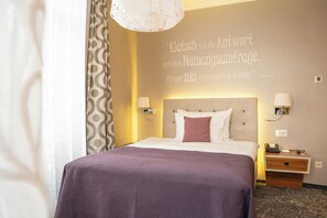 A hotel room with a bed, bedside lamps, a nightstand, and a wall quote. - Schweizerhof (Lucerne)