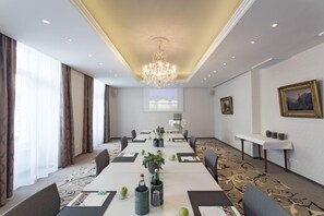 Un salón de conferencias con una larga mesa, sillas, una araña y cuadros en las paredes.