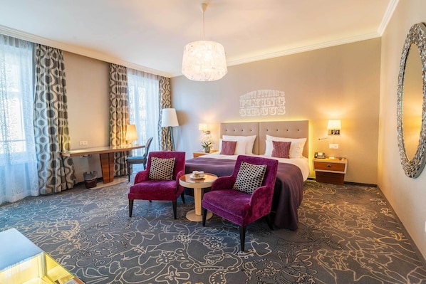 Habitación de hotel con una cama grande, dos sillones, una mesita y un candelabro.