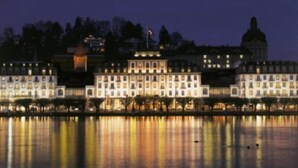 A waterfront hotel with multiple buildings, a flag, and a reflection on the water. - Schweizerhof (Lucerne)