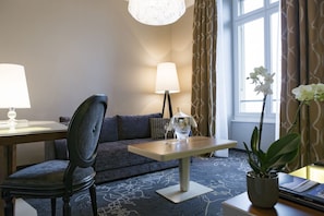 A hotel room with a sofa, a table with a bottle of champagne, a chair, a lamp, and a potted plant. - Schweizerhof (Lucerne)