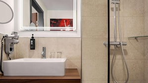 Un baño con un lavamanos blanco, un cabezal de ducha de mano y un espejo con luz.