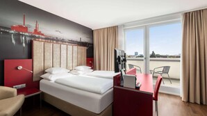 Una habitación de hotel con cama, escritorio, silla y una ventana grande con cortinas.