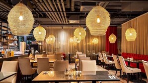 Interior de restaurante con mesas redondas, sillas y lámparas colgantes tejidas.