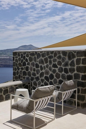 A stone wall with a white metal chair and a small white stool. - Apanemo Hotel and Suites (Santorini)