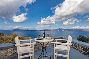 A table with two chairs and a bottle of wine, overlooking a scenic view of a body of water and distant mountains. - Apanemo Hotel and Suites (Santorini)