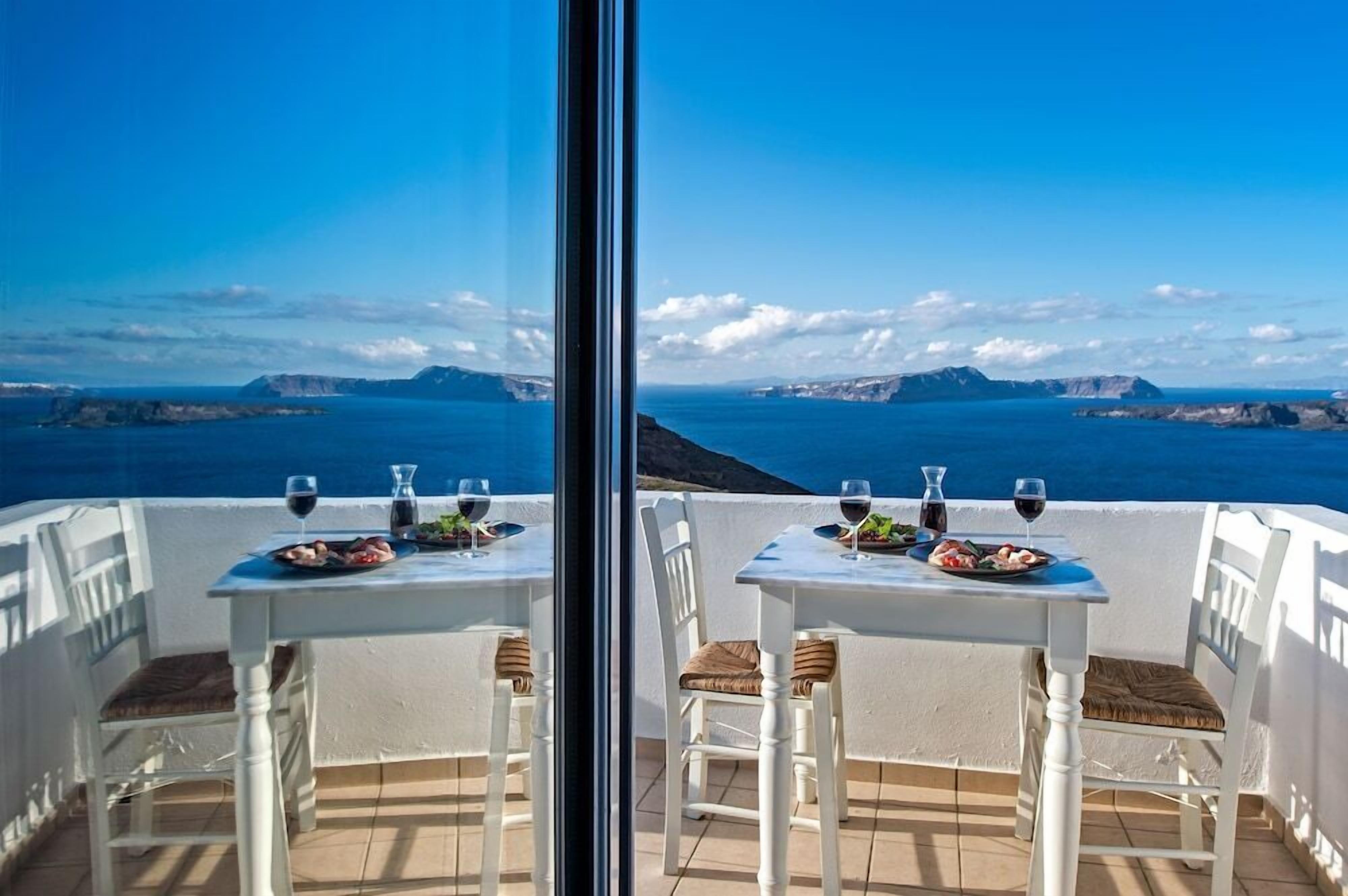 Un comedor con dos mesas, cada una con mantel blanco, dos sillas y vistas al mar y a islas distantes.