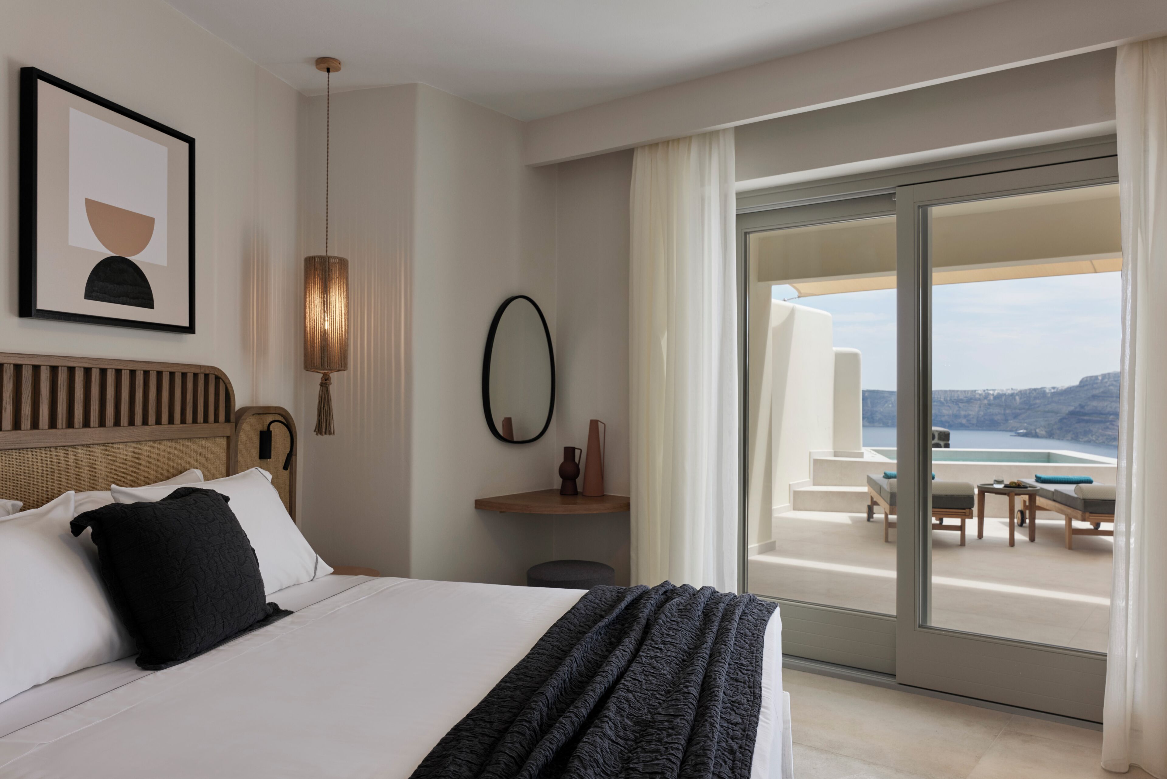 A hotel room with a bed, a large window with a view of the sea, a small table, and a chair.