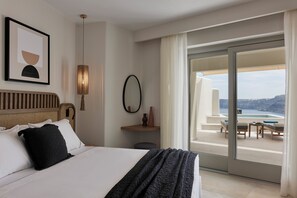 A hotel room with a bed, a large window with a view of the sea, a small table, and a chair. - Apanemo Hotel and Suites (Santorini)