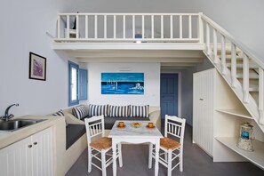 Ein kleines Zimmer mit Küchenzeile, einem Essbereich mit Tisch und Stühlen, einer Couch, einem Gemälde und einer Treppe.