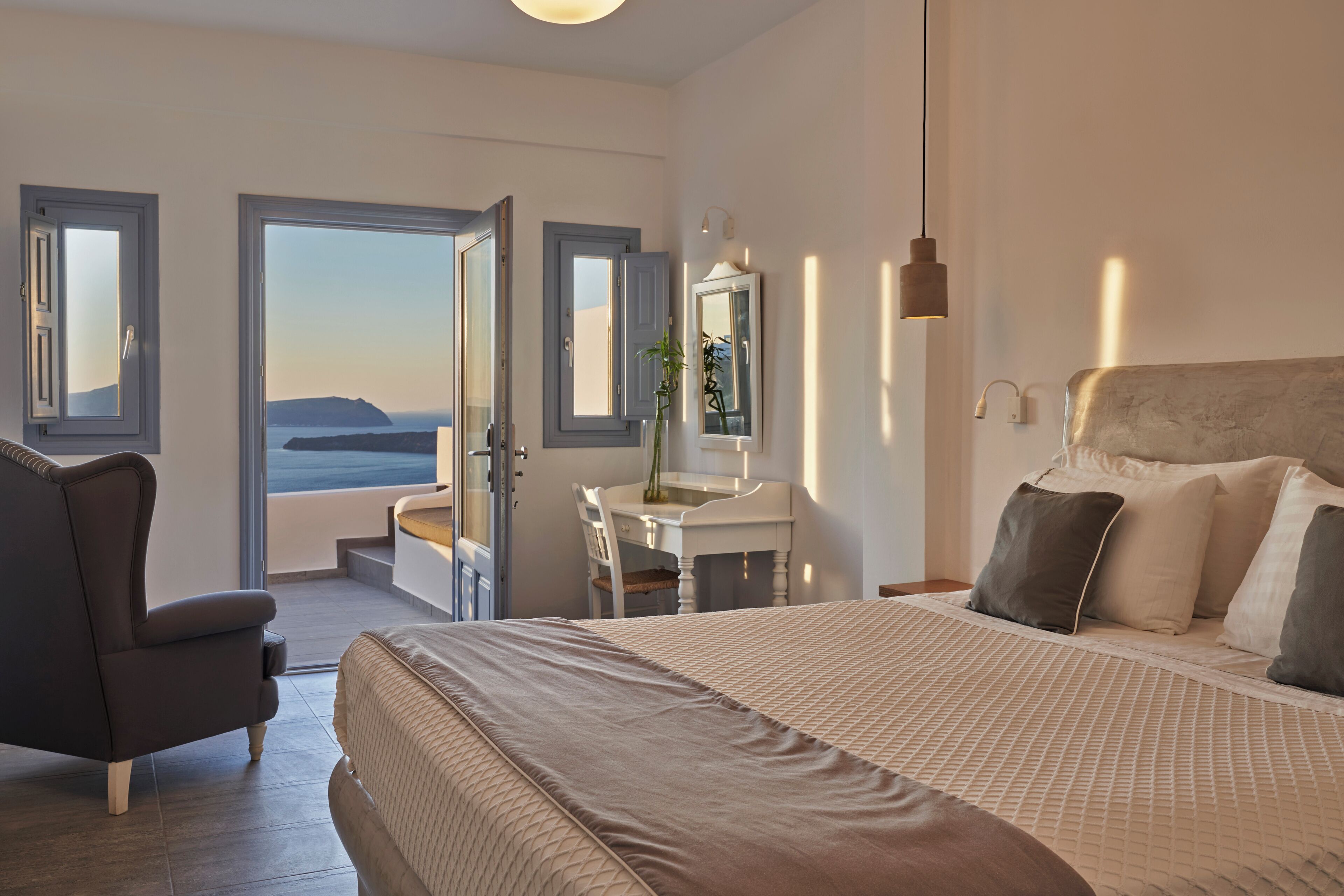 A bedroom with a bed, a chair, a desk, and a view of the sea.