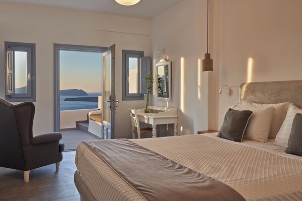 A bedroom with a bed, a chair, a desk, and a view of the sea. - Apanemo Hotel and Suites (Santorini)