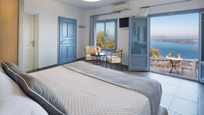 Un dormitorio con una cama grande, una pequeña mesa con sillas y un balcón con vista al mar.
