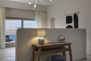 A modern room with a view of a snowy landscape, a wooden desk with a lamp, a chair, and a round mirror. - Apanemo Hotel and Suites (Santorini)