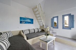 A modern living room with a sofa, a coffee table, a painting, and a staircase. - Apanemo Hotel and Suites (Santorini)