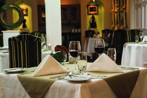 Una mesa de restaurante preparada con mantel verde, servilletas blancas y copas de vino.