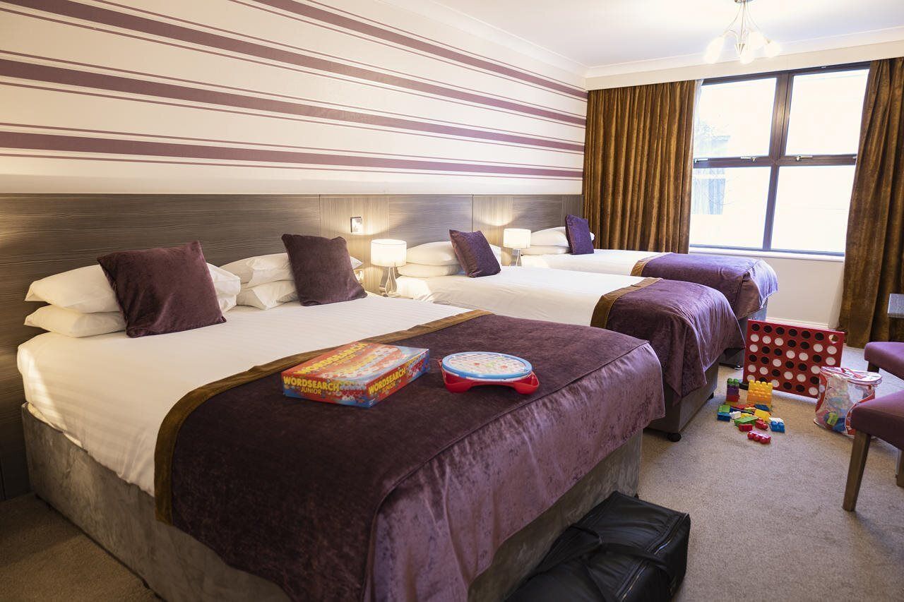 A hotel room with two beds, a window with curtains, and a small table with toys and books.