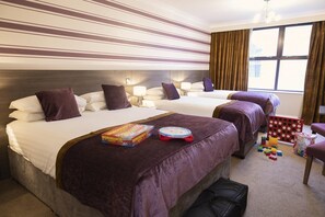 Una habitación de hotel con dos camas, una ventana con cortinas y una pequeña mesa con juguetes y libros.