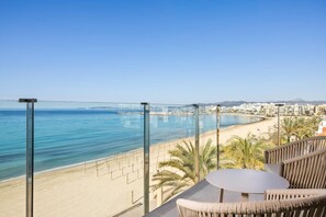 Un balcon offrant une vue dégagée sur une plage et l’océan, une table ronde et des meubles en osier.