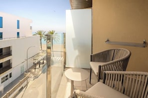 A balcony with a glass partition, a white refrigerator, wicker chairs, and a small round table. - Hotel Playa Mallorca (Palma de Mallorca)
