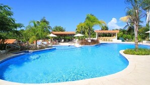 A swimming pool with a curved edge, surrounded by palm trees and lounge chairs. - Sugar Cane Club Hotel & Spa (Speightstown)