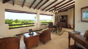 A room with wicker furniture, a dining area, and a view of greenery. - Sugar Cane Club Hotel & Spa (Speightstown)