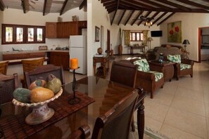 A spacious living area with a wooden dining table, chairs, and a kitchen in the background.