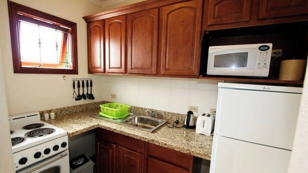 A kitchen with wooden cabinets, a microwave, a stove, and a sink. - Sugar Cane Club Hotel & Spa (Speightstown)