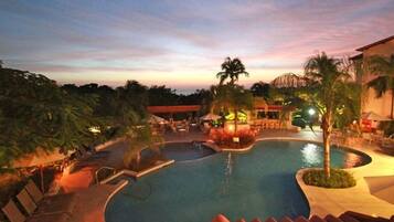 A swimming pool with a curved design, surrounded by palm trees and lounge chairs, indicating a resort setting.