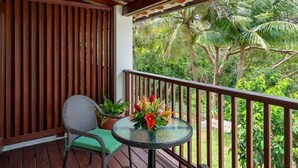 A balcony with a wicker chair, a small round table with a flower vase, and a view of tropical greenery. - Sugar Cane Club Hotel & Spa (Speightstown)