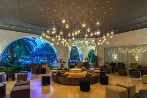 A lobby with a circular seating area, multiple hanging light fixtures, and a large arched window with a tropical view. - Hotel Tui Blue Oceana Suites (Hammamet)