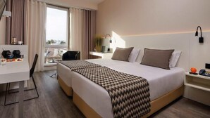 A hotel room with a bed, a desk, a chair, a window with curtains, and a nightstand with a lamp. - Hotel Faro and Beach Club (Faro)