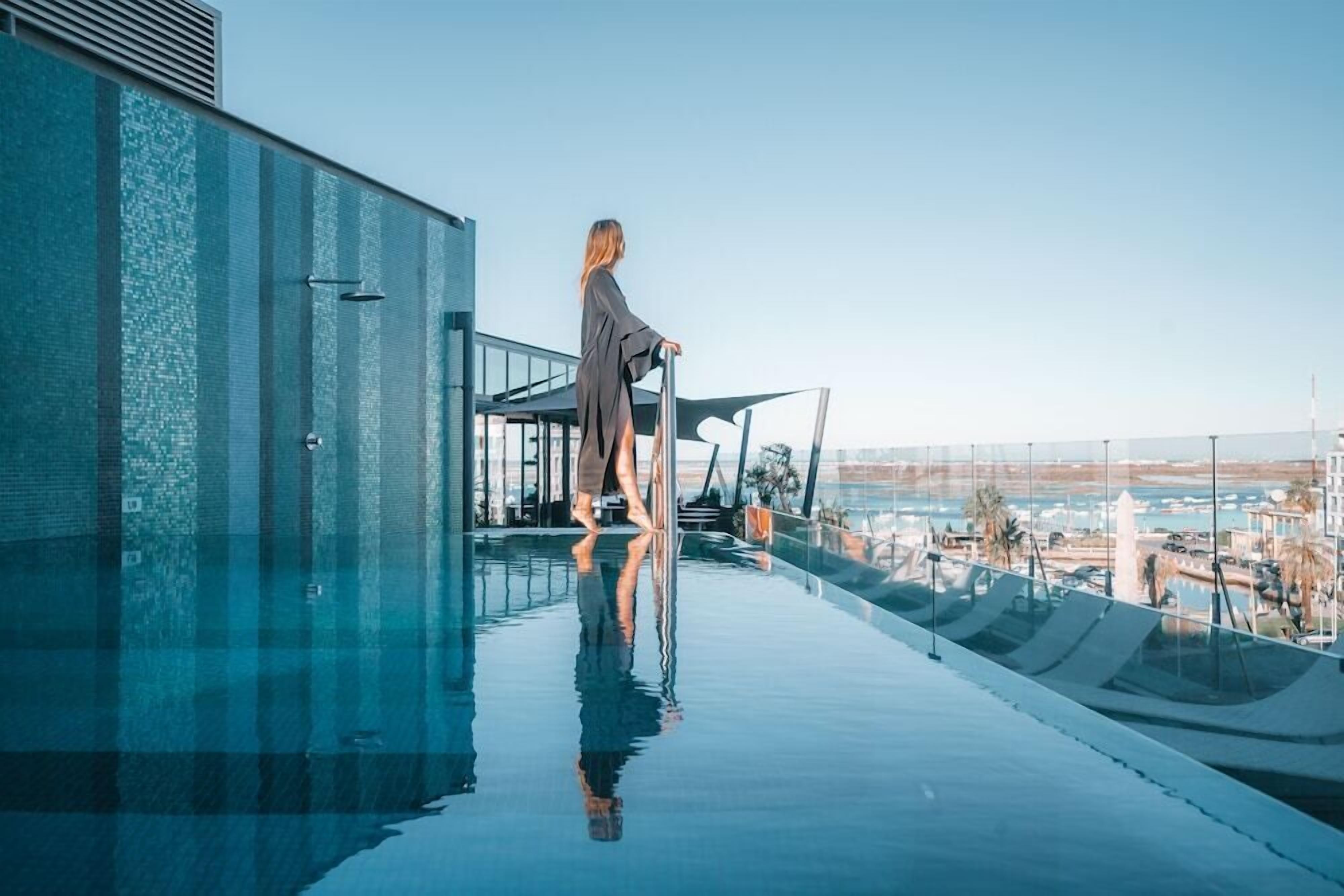 A person standing by a glass infinity pool with a city view.