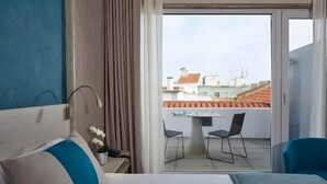 A hotel room with a bed, a desk, and a view of the cityscape through a glass door. - Hotel Faro and Beach Club (Faro)