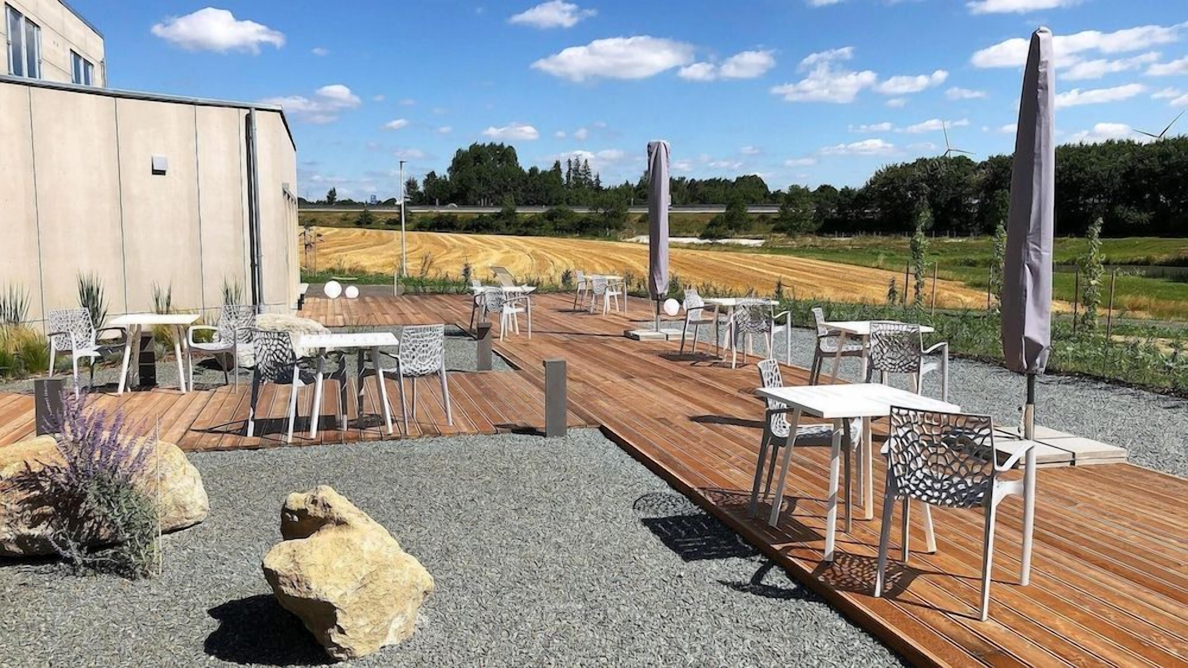 Un patio al aire libre con mesas y sillas, una terraza de madera y vista a un campo.