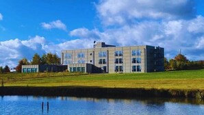 A modern building with multiple floors, large windows, and a flat roof, situated near a body of water. - The Bricks Hotel Marktredwitz (Marktredwitz)