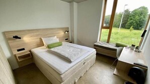 A bedroom with a bed, bedside tables, a desk, and a window with a view of greenery. - The Bricks Hotel Marktredwitz (Marktredwitz)