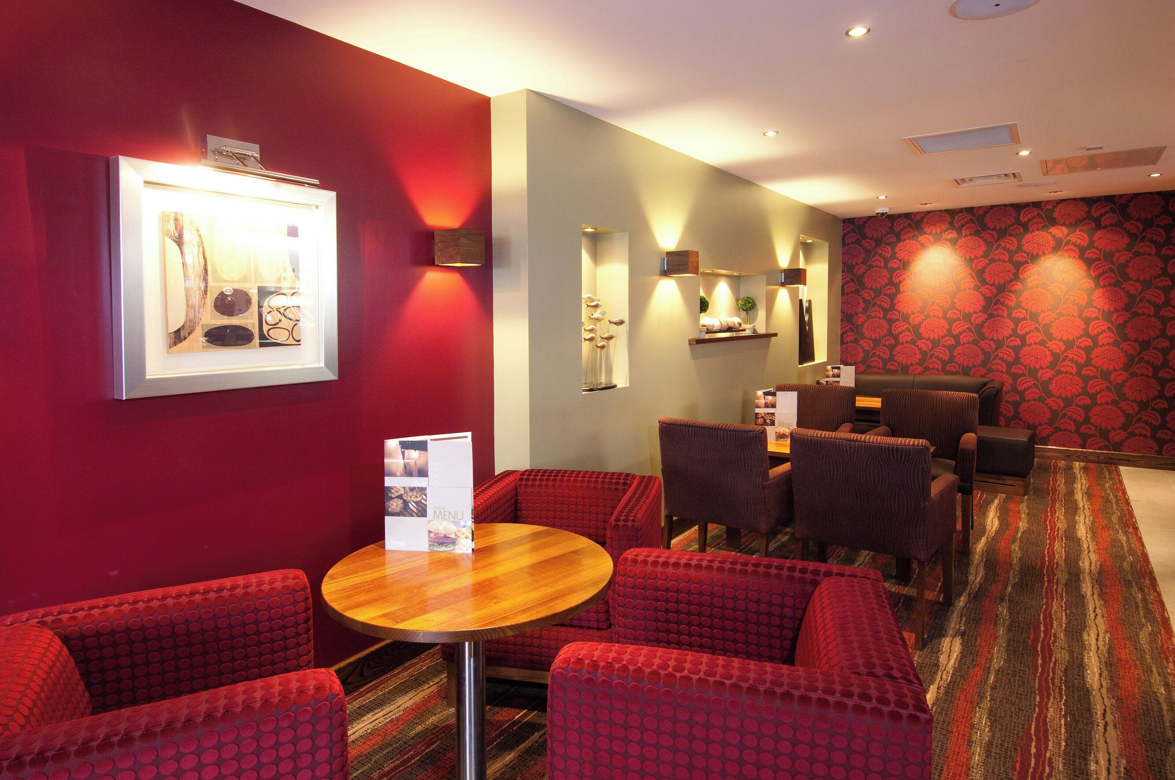 A hotel room with a red wall, a wooden table, and red patterned chairs.