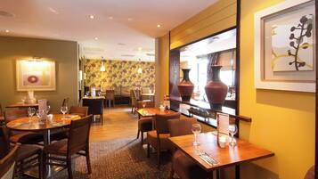 A restaurant with multiple dining tables and chairs, a patterned wall, and a large vase on display.