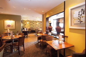 A restaurant with multiple dining tables and chairs, a patterned wall, and a large vase on display. - Premier Inn Sunbury (Sunbury on Thames)