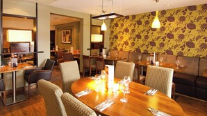 A restaurant with round tables, chairs, and a patterned wall. - Premier Inn Sunbury (Sunbury on Thames)